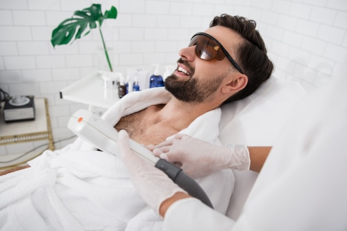 bearded man sitting in laser safety goggles in spa salon