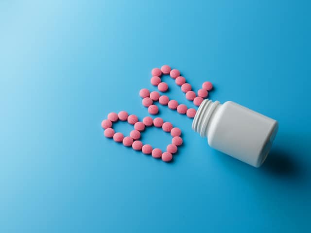 Pink pills in the shape of the letter B12 spilled out of a white can.